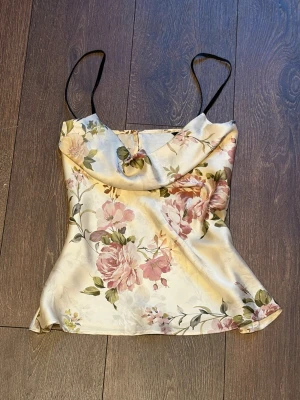 Blommig satinlinnetopp med tunna band - Söt och vacker topp / linne / blus med, sitter jättefint på! Väldigt unik, från Zara. 💕Har knappar i ryggen och är gjord av glansigt satin material. Toppen har tunna axelband och en lätt draperad urringning. Perfekt för sommarens alla tillfällen och ger en romantisk vibe.