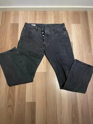 Svarta raka jeans från Levi's - Säljer ett par svarta raka jeans från Levi's med klassisk femficksdesign och knappgylf. Jeansen har en vintage vibe och är tillverkade i kraftig denim. Perfekta för dig som gillar en avslappnad och tidlös stil.