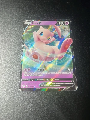 Pokémonkort Mew V holografisk - Säljer ett holografiskt Pokémonkort med Mew V, 180 HP. Kortet har en glittrig yta och motivet visar Mew i rosa och blå toner. Text och detaljer på engelska. Perfekt för samlare eller Pokémonfans.