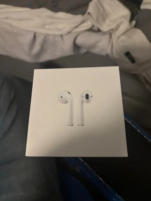 Apple AirPods trådlösa hörlurar - Säljer ett par vita Apple AirPods med klassisk stilren design. Hörlurarna är trådlösa och har en slimmad form som passar perfekt i öronen. Kommer i originalförpackning och är tillverkade i tålig plast. Perfekta för musik, poddar och samtal.