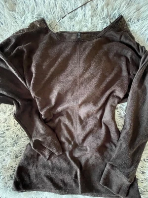 Brun tröja med paljettdetaljer - Mysig brun långärmad tröja med snygga paljettdetaljer på axlarna. Tröjan har en något figurnära passform och är tillverkad i ett mjukt material som känns skönt mot huden. Perfekt för dig som vill ha något extra till din outfit.
