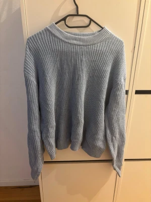 Ljusblå stickad tröja från 157 - Snygg ljusblå stickad tröja från 157 med grovstickad struktur och rund halsringning. Perfekt för lager-på-lager och enkel att matcha med jeans eller kjol. Tröjan har långa ärmar och avslappnad passform.