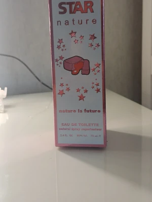 Star Nature Eau de Toilette 70 ml - Säljer en parfym från Star Nature, Eau de Toilette i en rosa och vit förpackning med stjärnmotiv. Flaskan innehåller 70 ml och har en söt, ungdomlig design. Perfekt för dig som gillar fräscha och lekfulla dofter.