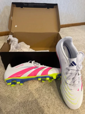 Adidas Predator vita fotbollsskor - Snygga Adidas Predator fotbollsskor i vitt med neonrosa och gula detaljer. Skorna är helt splitternya och köptes på unisport för 800kr Priset ej fast så kom med bud 👍