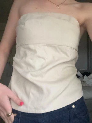 Beige tubtopp  - Snygg beige tubtopp med bandeau-modell. Perfekt att styla med jeans eller kjol för en trendig look. Toppens material har en lätt ribbad struktur och sitter tajt över bysten. Lite shimmerig