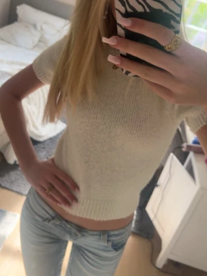 Vit stickad topp från Gina Tricot - Superfin vit stickad topp från Gina Tricot med korta ärmar och ribbade detaljer vid ärmslut och midja. Perfekt till jeans eller kjol för en fräsch look. Enkel och stilren design som passar till mycket.