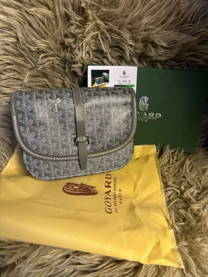 Grå axelväska med monogram - Snygg grå handväska  med klassiskt monogrammönster och detaljer i läder. Väskan har lock med spänne framtill och kommer med original dustbag och förpackning. Perfekt för dig som gillar exklusiva accessoarer och tidlös design.