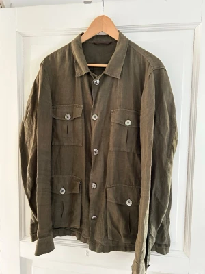 Oscar Jacobson Safari Jacket - Mörkgrön Oscar Jacobson Safari Shirt Jacket i 100% linne. Nyskick, strl L.  Säljes då den inte kommer till användning.   Nypris: 2499 kr  Modell: Safari Shirt Jacket  Material: 100% Linne Färg: Mörkgrön  Passform: Regular  Tillverkad: Bulgarien 
