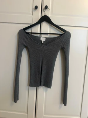 Grå ribbad långärmad topp - Snygg grå ribbad topp från H&M med v-ringning och lång ärm. Modellen är figurnära och har en djupare urringning framtill. Perfekt att styla med jeans eller kjol för en trendig look.