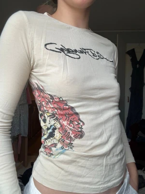 Ed Hardy långärmad topp – beige med grafiska tryck - Fint skick! Säljes då den är för liten för mig! Storlek M men väldigt liten i storleken isåfall! Made in portugal 