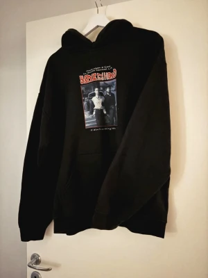 Svart Boys n the Hood hoodie - Svart hoodie med tryck av filmen Boys n the Hood på bröstet. Sorlek M/L. Klassisk passform med huva och känguruficka framtill. Perfekt för dig som gillar streetwear och filmreferenser. Mjuk bomullskänsla och coolt motiv i svartvitt med röda detaljer.
