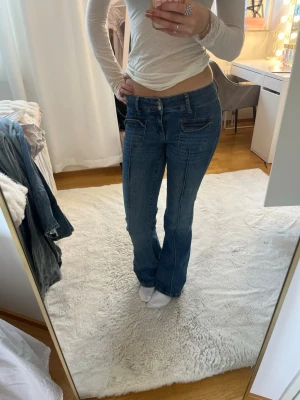 Blå low waist bootcut jeans - Säljer ett par blå low waist jeans med bootcut-modell och markerade sömmar. Jeansen har stora fickor fram och bak samt en knappgylf. Perfekta för dig som gillar en retro vibe och vill ha ett par jeans som sticker ut lite extra. 