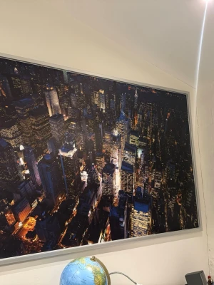 Tavla med nattvy över New York - Stor tavla med ett färgstarkt fotografi av New York i nattljus. Bilden visar skyskrapor och stadens ljus i mörka toner med inslag av gult, blått och vitt. Tavlan har en smal, ljus ram och passar perfekt som väggdekoration. Längd: 200cm. Höjd: 140cm