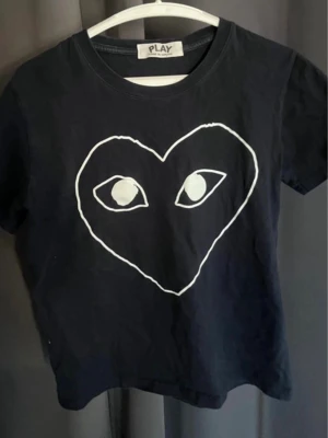 Marinblå Comme des Garçons PLAY t-shirt - Marinblå t-shirt från Comme des Garçons PLAY med ikoniskt vitt hjärta med ögon tryckt på bröstet. Klassisk rund halsringning och korta ärmar. Tillverkad i mjuk bomull som känns skön mot huden. Perfekt för dig som gillar streetwear och grafiska prints.
