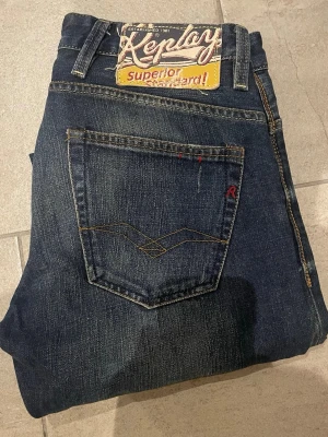 Mörkblå jeans från Replay - Snygga mörkblå jeans från Replay med raka ben och klassisk femficksmodell. Jeansen har slitningar och kontrastsömmar samt en stor Replay-patch bak i midjan. Materialet är denim i bomull med en cool vintagekänsla.