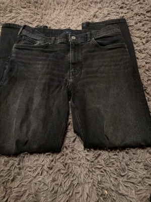 Svarta jeans från GANT - Säljer ett par svarta jeans från GANT med klassisk femficksmodell och raka ben. Jeansen har en diskret tvättad look och är tillverkade i mjukt denimtyg. Passar perfekt till en avslappnad stil och har GANT-logga på bakfickan. Sista bilden kan vara rätt så oklar men det står att det passar dig som är 158-164 eller 13-14 år
