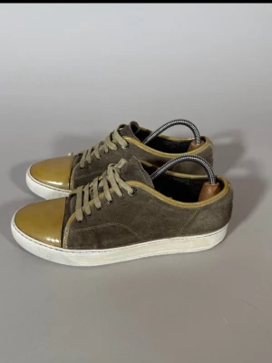 Olivgröna sneakers med mocka och lack - Snygga sneakers i olivgrön mocka med glansig guldfärgad lack på tån och vita sulor. Skorna har klassisk låg profil, matchande olivgröna skosnören och en stilren design som sticker ut. Perfekta för dig som vill ha något unikt till din outfit.