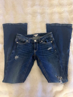 Blå bootcut jeans med slitningar från ginatricot TALL - Snygga blå bootcut jeans med slitningar och ljusa tvättade detaljer från ginatricot TALL. Jeansen har vita kontrastsömmar och broderade bakfickor. Klassisk femficksmodell och låg midja. Perfekta för en avslappnad och trendig look. Har defekter vid hälarna kan ses på sista bilderna. Nypris 399.