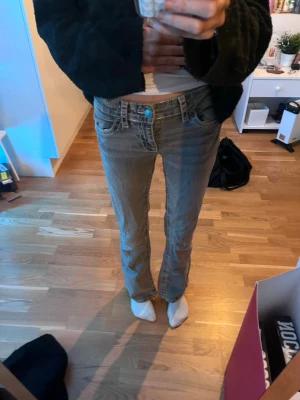 Grå bootcut jeans med kontrastsömmar - Säljer ett par grå bootcut jeans med vita kontrastsömmar och snygga detaljer på bakfickorna. Jeansen har låg midja, klassisk femficksmodell och metallknappar. Perfekta för dig som gillar en avslappnad men ändå trendig look💕