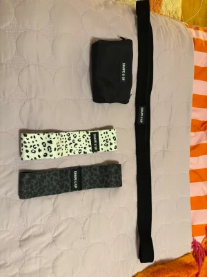 Träningsband Shape U Up set - Säljer ett set med träningsband från Shape U Up. Setet innehåller tre olika motståndsband i tyg, ett svart, ett grått med leopardmönster och ett vitt med svart leopardmönster samt en svart förvaringspåse. Perfekt för hemmaträning eller gymmet.