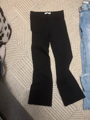 Svarta bootcut jeans från Gina Tricot - Snygga svarta bootcut jeans från Gina Tricot med klassisk femficksdesign och utsvängda ben. Jeansen har en hög midja och är tillverkade i stretchigt denimtyg som sitter bekvämt. Perfekta för dig som vill ha en trendig siluett.