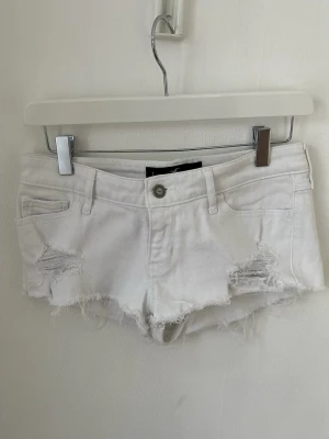 Vita Jeans shorts från Hollister - Säljer ett par vita denimshorts från Hollister med låg midja och detaljer framtill. Perfekta för sommaren och är jätte fina med en stickad tröja.