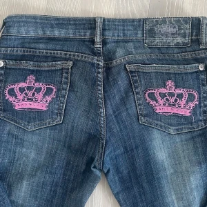 Blå jeans med rosa kronbrodyr - Snygga bootcut jeans med Victoria Beckhams signatur kronor. Dessa rosa kronor är väldigt eftersökta! 🩷🩷Brodering på ena fickan sitter löst men det är inget problem och syns endast om du tittar noga☺️storlek 29, passar mig som är S perfekt. Mina bilder!! Kommer lägga ut på Vinted för samma pris💕