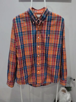  Yves Saint Laurent skjorta  - Färgglad rutig skjorta från Yves Saint Laurent med klassisk krage och knäppning framtill. Skjortan har lång ärm och broderad YSL-logga i gult på bröstet. Materialet känns som bomull och färgerna är orange, blå, grön och röd.