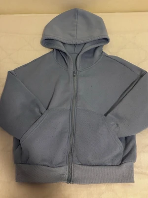 Ljusgrå zip hoodie med huva - En stilren ljusgrå hoodie med dragkedja framtill och stor känguruficka. Hoodien har en klassisk huva och ribbade muddar vid ärmslut och nederkant. Perfekt för en avslappnad look och enkel att matcha med andra plagg.hoodien är cropped 