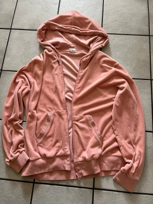 Rosa zip-hoodie med fickor storlek 48/50 - Mysig rosa hoodie med dragkedja framtill och två stora fickor. Tröjan har huva och ribbade muddar vid ärmslut och nederkant. Perfekt för en avslappnad stil. Materialet känns mjukt och bekvämt.