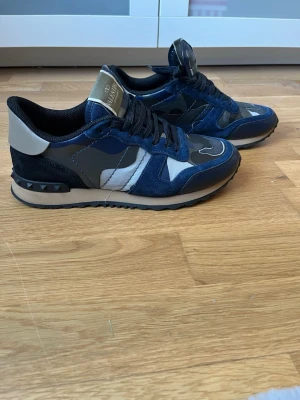 Valentino rockrunners - Snygga sneakers från Valentino med blått camo-mönster, svarta och grå detaljer samt vita inslag. Skorna har svarta skosnören, beige sula och nitar på hälen. Materialmix av mocka, textil och läder ger en exklusiv känsla. Perfekta för dig som vill sticka ut med stil. Stl 40 1/2 lite större i stl .