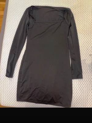 Svart långärmad klänning - En enkel och stilren svart klänning med lång ärm och rak passform. Klänningen har en offshoulder-design som ger en trendig look. Perfekt för dig som gillar minimalistisk stil.