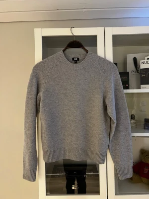 Ljusgrå stickad tröja från Uniqlo - En snygg, grå, stickad tröja från uniqlo. Helt oanvänd och riktigt fräsch. Tröjan är ull och har en ribbad hals samt en normal passform.