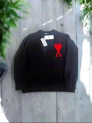 Svart stickad tröja från Ami - Snygg svart stickad tröja från Ami Alexandre Mattiussi med röd hjärtlogga och bokstaven A på bröstet. Tröjan har ribbade muddar vid hals, ärmslut och nederkant. Perfekt för dig som gillar stilrena plagg med en twist.