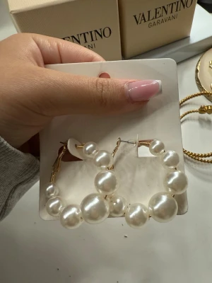 pärlörhängen i guld - Stora creolörhängen med vita pärlor i olika storlekar på guldfärgad metall. Perfekta för dig som vill ha ett statement-smycke med lyxig känsla och trendig design.