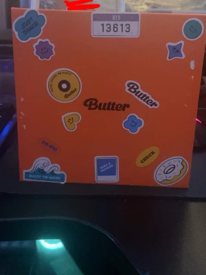 BTS Butter album peaches  - Säljer en BTS Butter album box i orange med flera färgglada klistermärken på framsidan. Boxen har tryck med texten 'Butter' och olika motiv som vågor, smileys och stjärnor. Perfekt för samlare av K-pop och BTS-merch. Original pris 322 