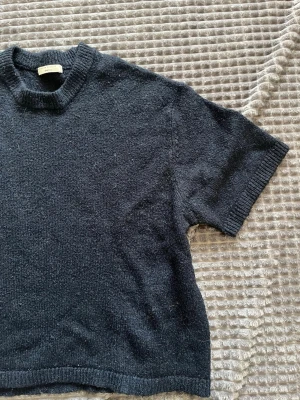 Mörkblå stickad t-shirt Hope - Kortärmad stickad t-shirt från Hope i mörkblått. Tröjan har ribbstickad halsringning, ärmslut och nederkant. Perfekt för dig som gillar en enkel men stilren look med en twist av stickat material.