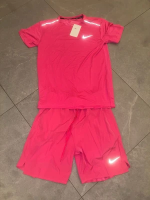 Rosa träningsset  - Säljer ett sportigt rosa träningsset med t-shirt och shorts. Båda plaggen  är tillverkade i ett lätt, snabbtorkande material som passar perfekt för träning. T-shirten har rund hals och korta ärmar, shortsen har dragsko i midjan.