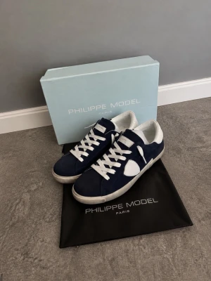 Philippe Model Low PRSX Mörkblå Suede - Snygga sneakers från Philippe Model i mörkblå mocka med vita detaljer och vita skosnören. Skorna har en klassisk låg siluett och vit sula. Perfekta för dig som gillar stilrena och trendiga sneakers med premiumkänsla. Nypris : 2800kr. Ny skick. Skorna har suede material. Box och Dustbag tillkommer. 