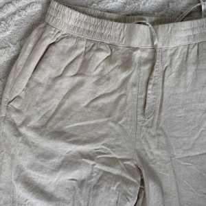 Beiga 50% linnebyxor med resårmidja - Säljer ett par ljusbeige linnebyxor med avslappnad passform och resår i midjan. Byxorna har snedställda fickor fram och två fickor med lock bak. Perfekta för en chill och stilren look. Materialet är svalt och luftigt linne.