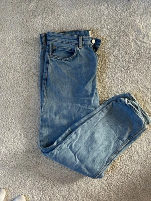 Blå jeans från Pull&Bear - Säljer ett par klassiska blå jeans från Pull&Bear i rak modell. Jeansen har fem fickor, bälteshällor och stängs med knapp och dragkedja. Tillverkade i bomull med en snygg tvättad look som passar till allt.