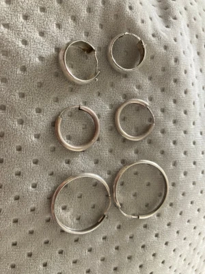 3 par silvriga hoops örhängen - Säljer tre par klassiska hoops örhängen i silver. Alla är runda och har enkel, stilren design i olika storlekar. Perfekta för dig som gillar minimalistiska accessoarer och vill kunna variera din look med olika storlekar på hoops.