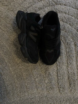 New balance 9060 - Säljer ett par helsvarta New Balance sneakers med chunky sula och klassisk N-logga på sidan. Skorna har en sportig design med mesh och mockadetaljer, samt svarta skosnören. Perfekta för dig som gillar streetwear och vill ha en stilren look.