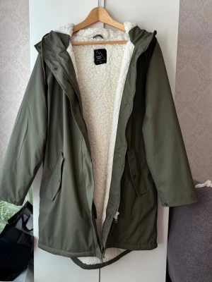Grön fodrad parkas   - Grön pilefodrad regnkappa från Mount Zero i strl M. Jackan har huva, dragkedja och knappar framtill samt två stora fickor. Knappt använd, mycket bra skick!❤️