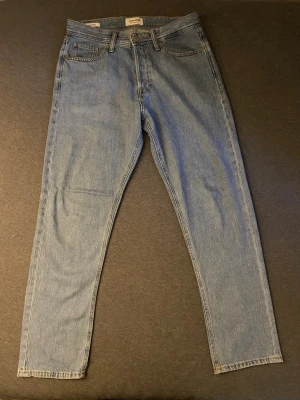 Blå jeans - Säljer ett par ljusblå mom jeans från Jack n Jones med klassisk femficksdesign och hög midja. Jeansen har raka ben och är tillverkade i ett mjukt denimtyg. Perfekta för en avslappnad och trendig look.