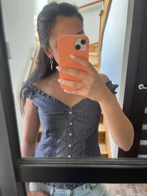 Mörkblå prickig offshoulder topp - Supersöt mörkblå offshoulder topp med vita prickar och knappar framtill. Toppen har volangdetaljer vid axlarna och en figurnära passform som framhäver midjan! Köpt i en brandy Melville liknade butik i newyork