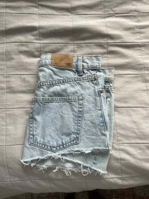 Ljusblå jeanskjol med rå kant - Ljusblå jeanskjol från 157 med klassisk femficksdesign, bälteshällor och rå, fransig kant nedtill. Kjolen har knappgylf och är gjord i ett slitstarkt bomullsmaterial. Perfekt för en avslappnad och trendig look.