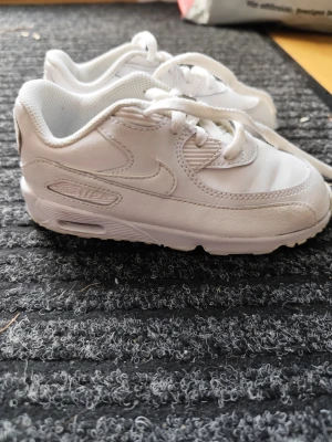 Vita Nike Air Max sneakers - Säljer ett par helvita Nike Air Max sneakers med klassisk chunky sula och ikonisk swoosh på sidan. Skorna har snörning, vadderad krage och är tillverkade i en mix av läder och textil. Perfekta för dig som gillar stilrena och sportiga sneakers.
