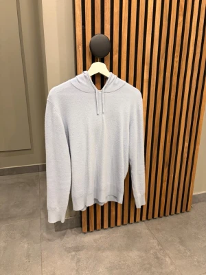 Kashmir hoodie - Mysig ljusblå hoodie med huva och dragsko. Tillverkad i ett mjukt, kashmir material som känns skönt mot huden. Hoodien har långa ärmar och ribbade muddar vid ärmslut och nederkant. Perfekt för en avslappnad och stilren look.