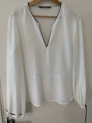 Zara blus - Stilren vit blus från Zara med lång ärm och svarta kontrastsömmar längs V-ringningen och vid ärmsluten. Blusen har en lös passform och tunnt, lätt material som ger ett luftigt intryck.  Pris går att diskutera 💗